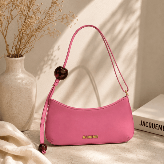 Bubblegum pink crescent shoulder bag with a smooth faux leather finish, decorative resin bead accents, adjustable shoulder strap, gold-tone hardware, and a minimalist curved silhouette displayed in a modern indoor setting.