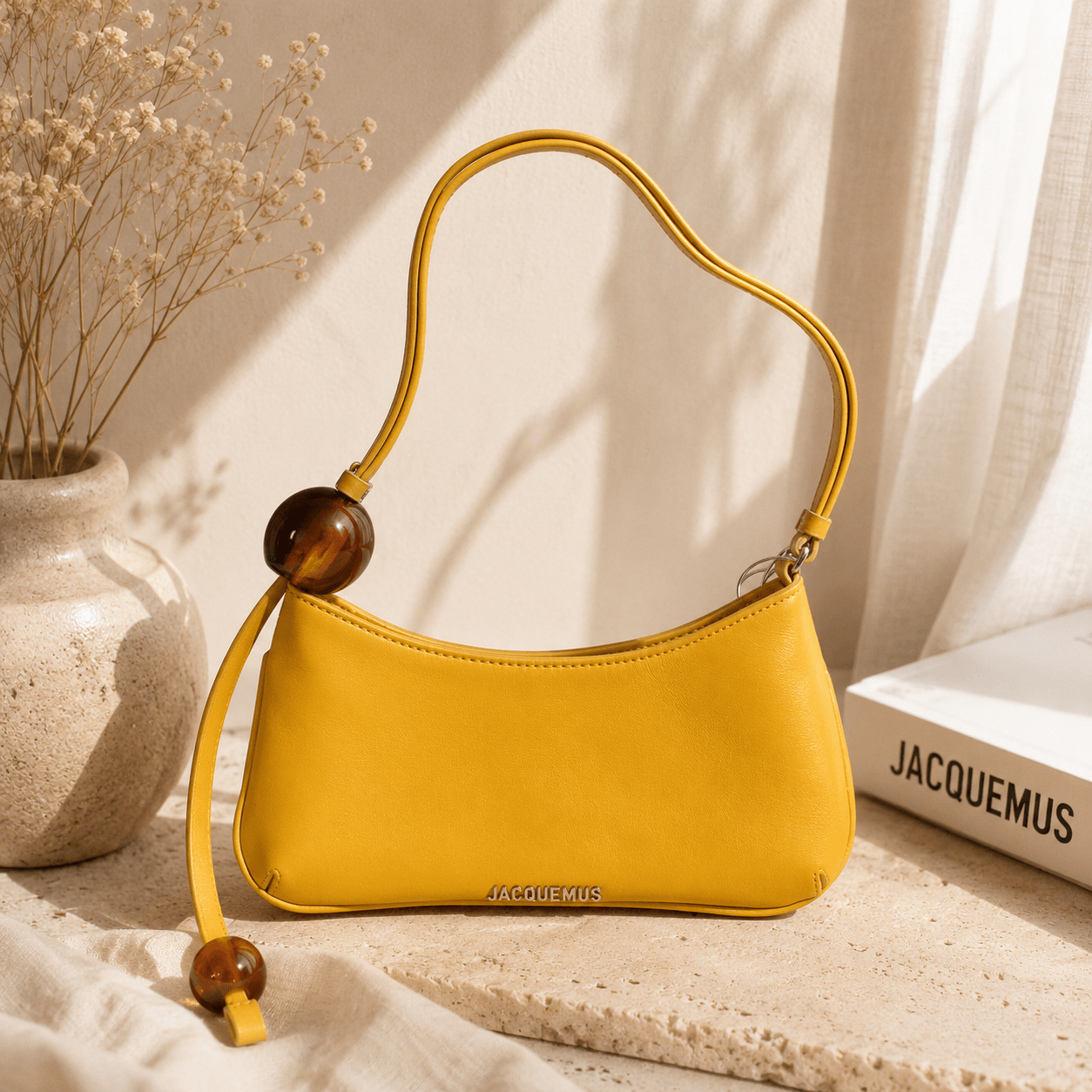 Mustard yellow crescent shoulder bag with a curved silhouette, smooth faux leather finish, decorative resin bead accents, adjustable shoulder strap, and minimalist everyday design displayed in a warm neutral lifestyle setting.