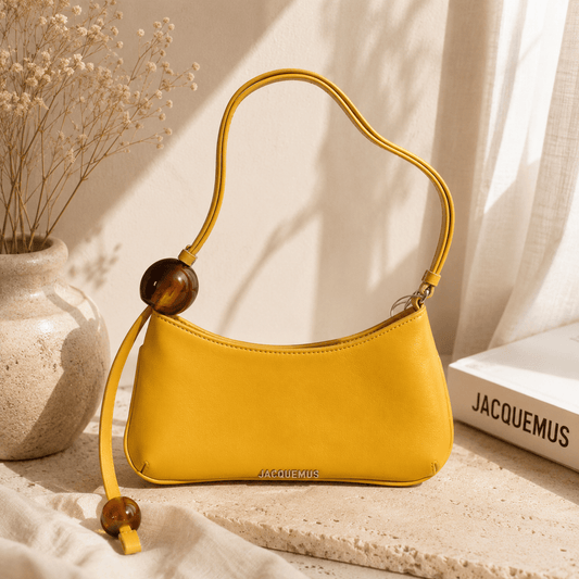 Mustard yellow crescent shoulder bag with a curved silhouette, smooth faux leather finish, decorative resin bead accents, adjustable shoulder strap, and minimalist everyday design displayed in a warm neutral lifestyle setting.