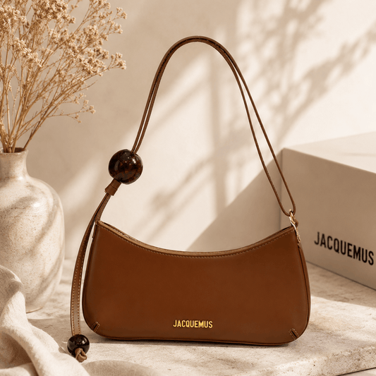 Vintage brown crescent shoulder bag made from smooth faux leather with glossy resin bead accents, an adjustable shoulder strap, gold-tone hardware, and a minimalist curved silhouette displayed in a warm modern lifestyle setting.